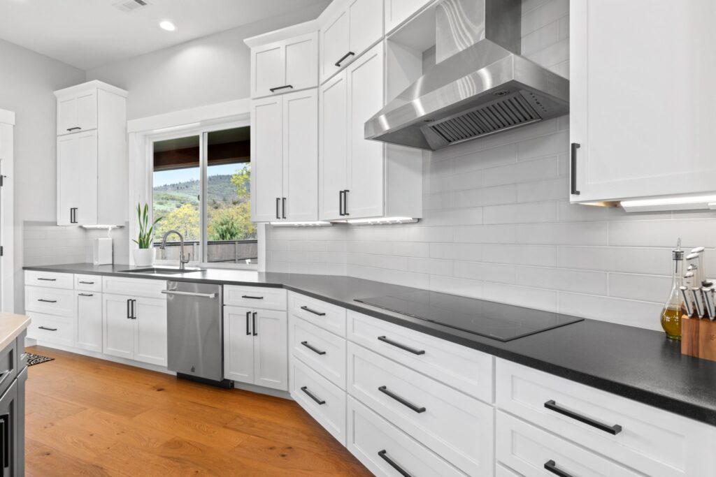 White kitchen cabinets with dark countertops and a stainless range hood