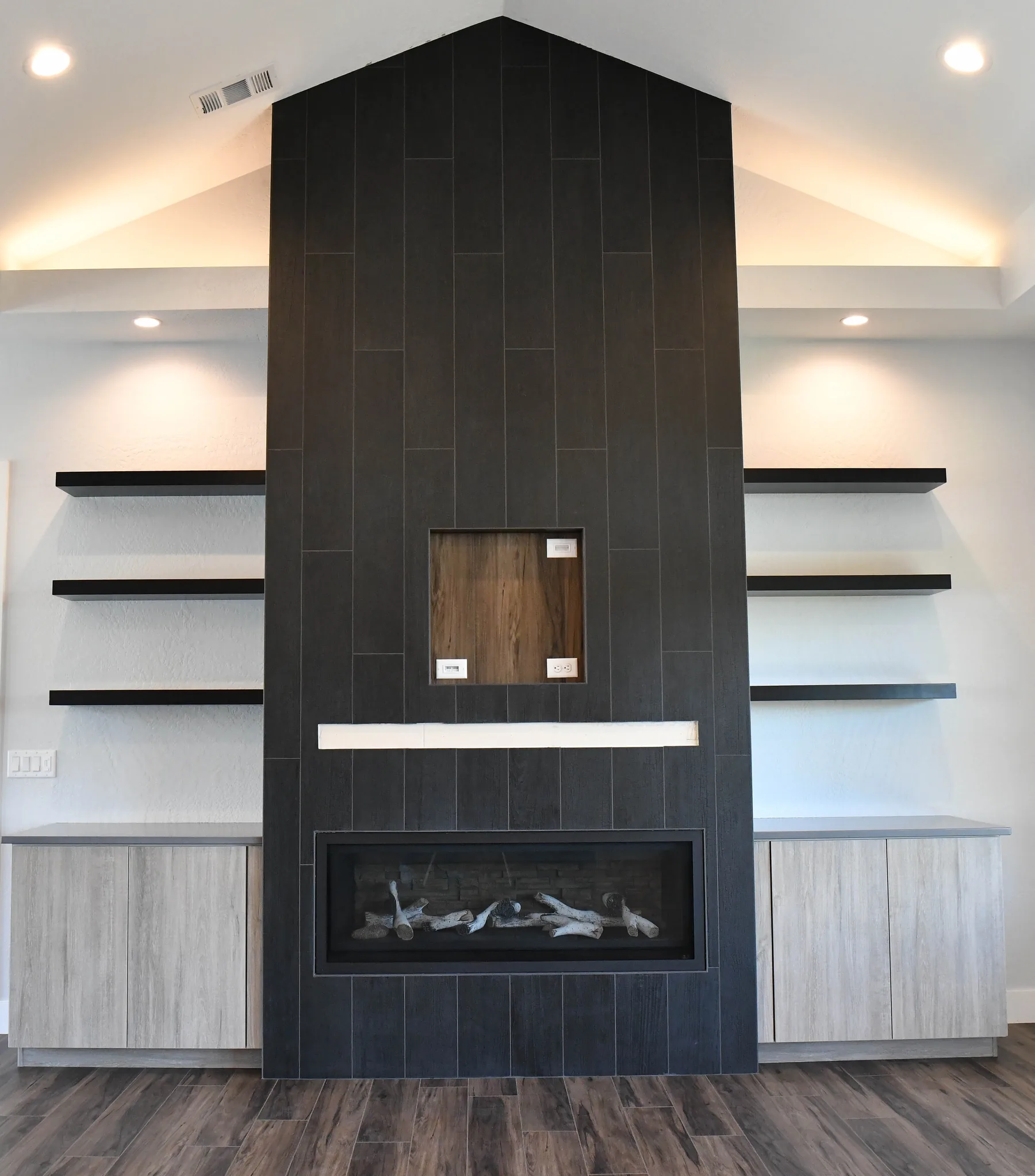 Black tiled fireplace with built-in floating shelves and lower cabinets