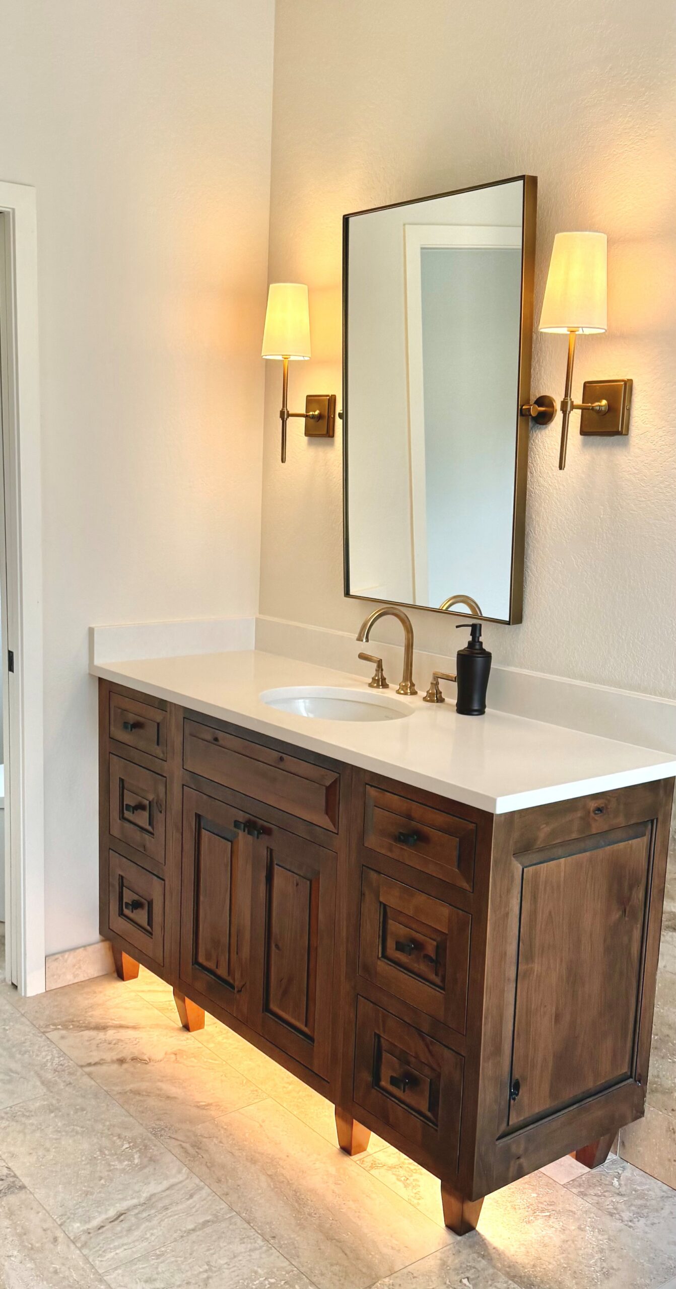 Dark wood bathroom vanity with a white countertop, black-framed mirror, and wall sconces