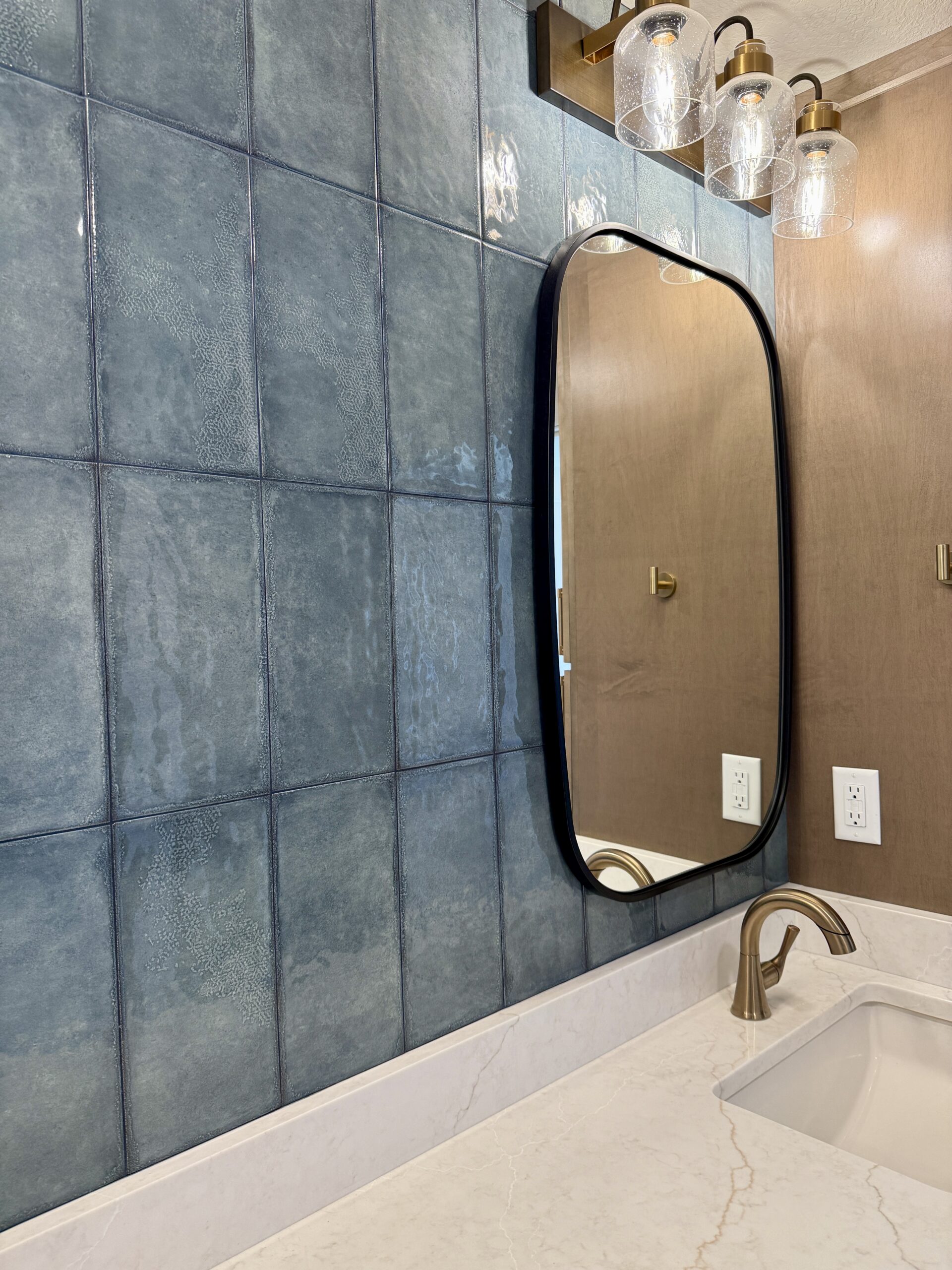 Blue square wall tile behind a black-framed bathroom mirror and white vanity countertop