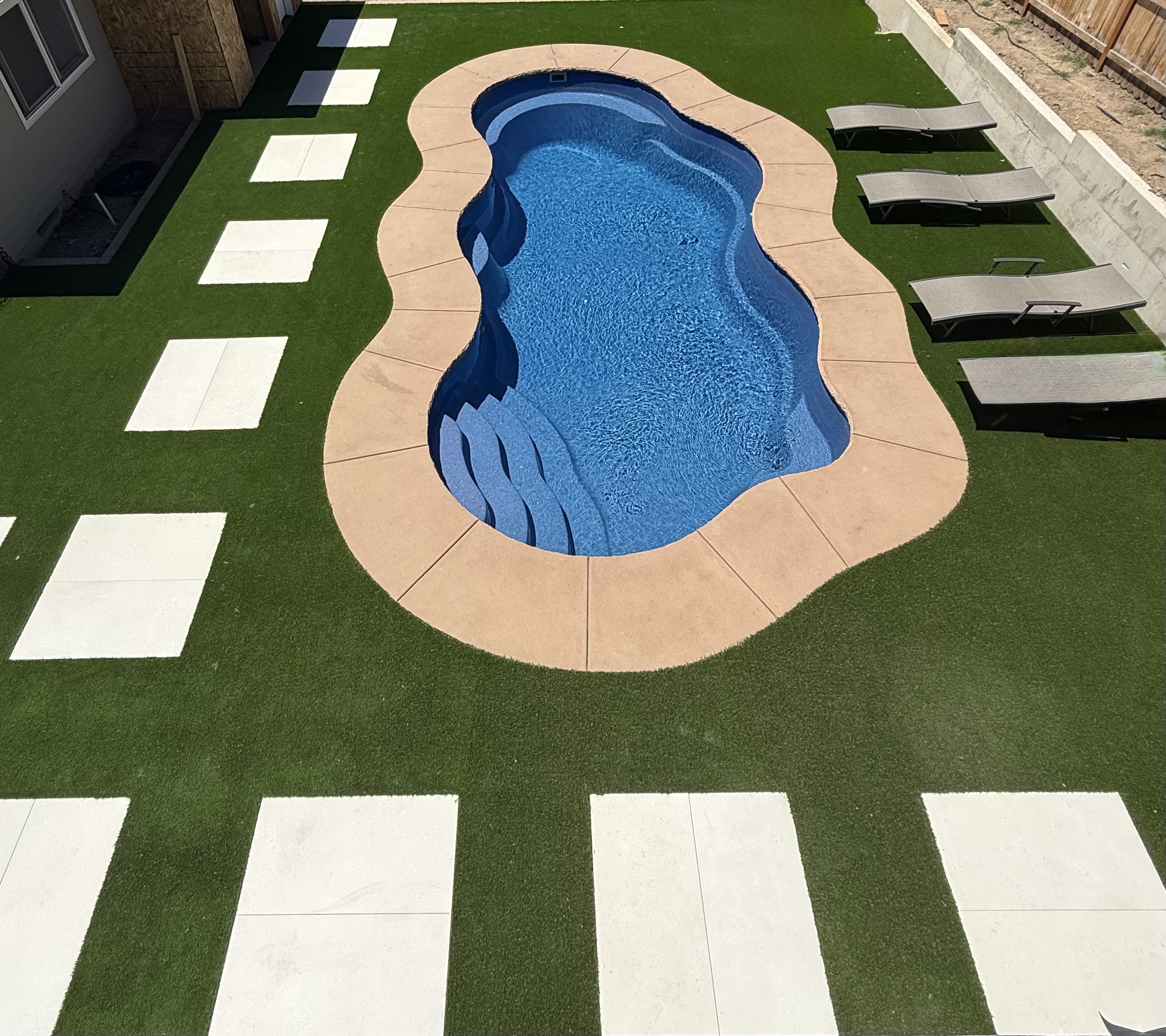 Backyard swimming pool surrounded by artificial turf and concrete pavers
